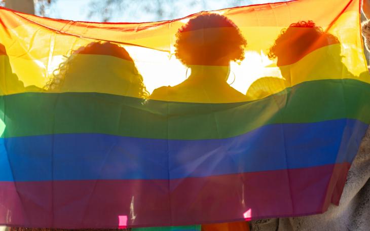 three women sit behind a pride flag