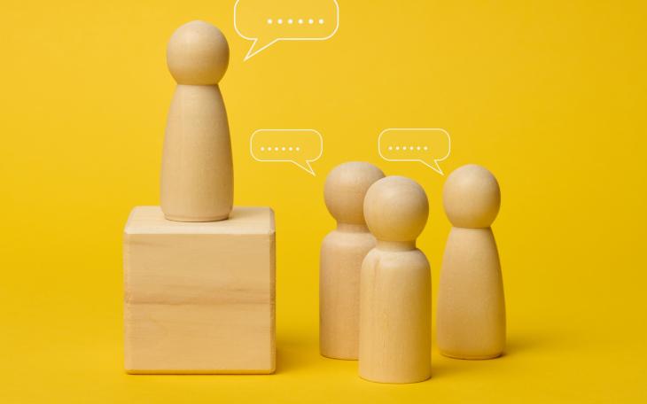 wooden figures with speech marks on yellow background