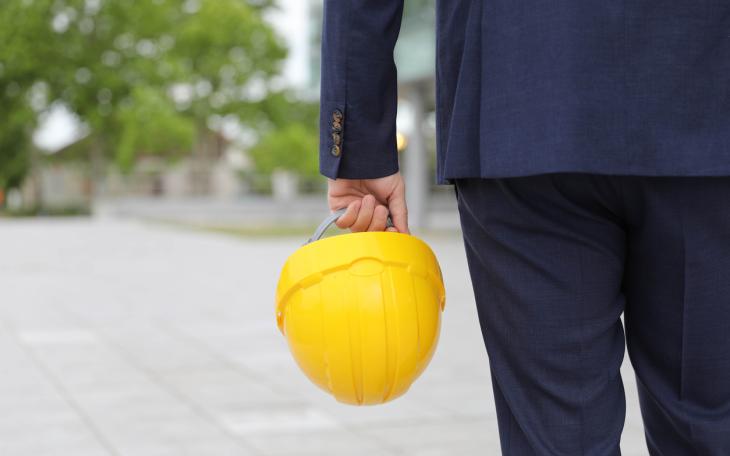 man in suit holds yellow hard hat