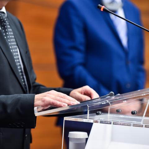 man at podium in suite speaks on a microphone