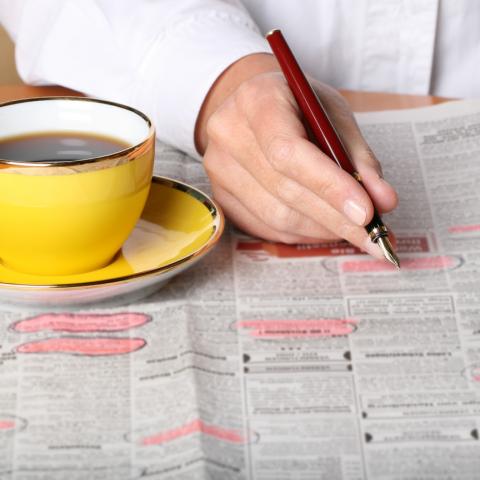 man circles job vacancies in the newspaper with yellow mug of coffee