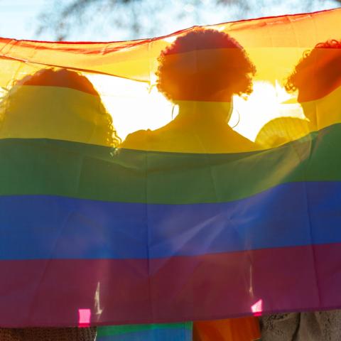 three women sit behind a pride flag
