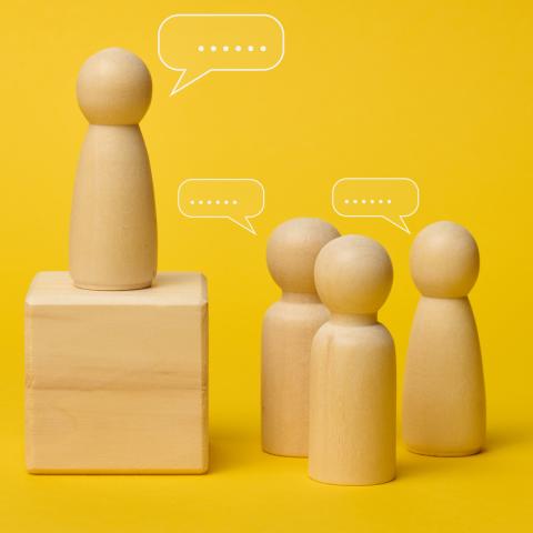 wooden figures with speech marks on yellow background