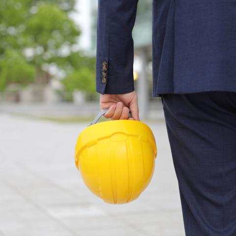 man in suit holds yellow hard hat