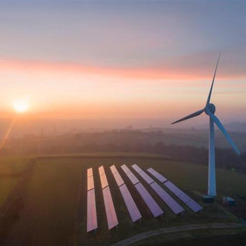 solar panels and wind turbine on a field at sunset